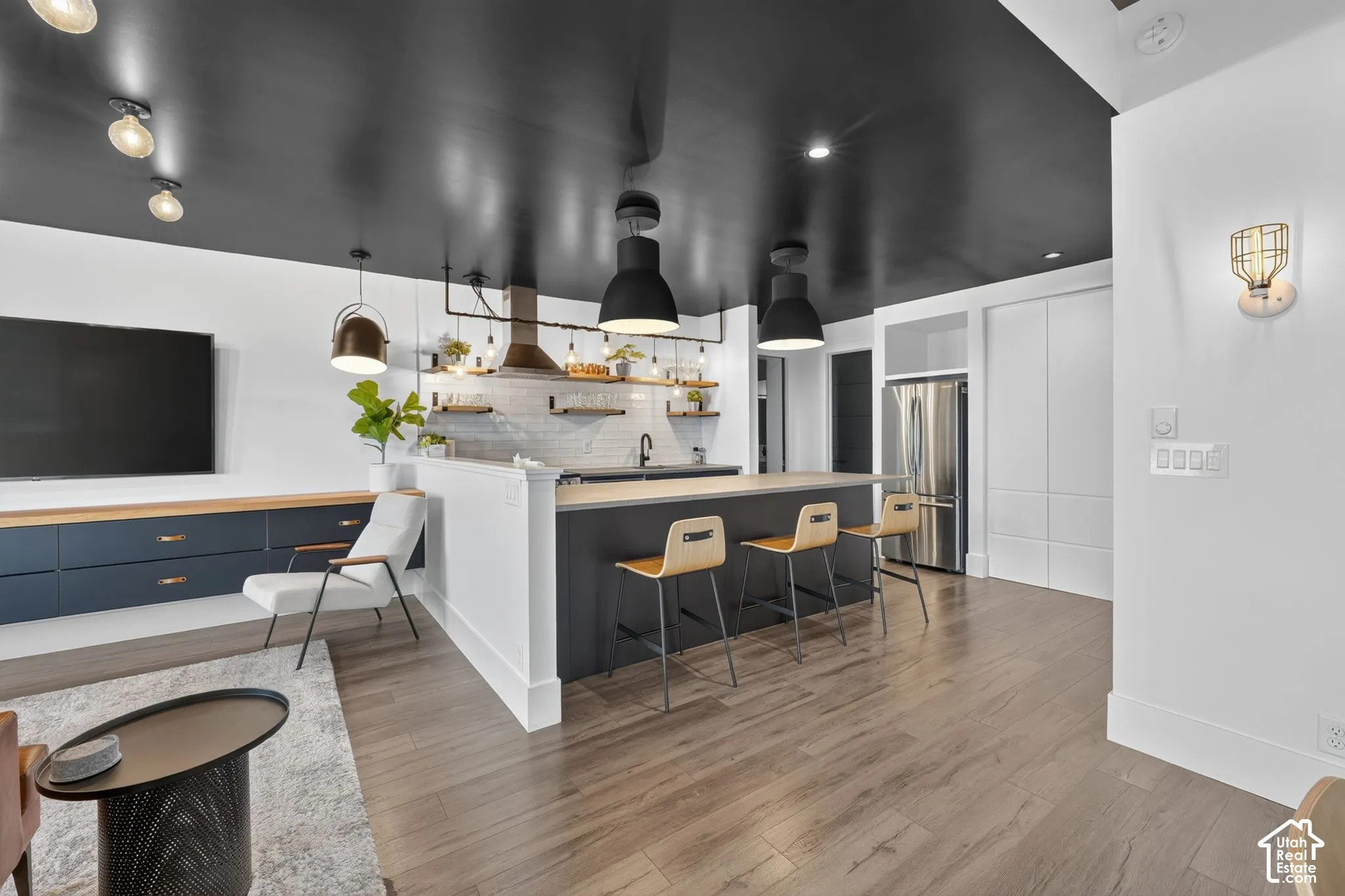 Open-concept living space featuring wood-finish flooring, a kitchen island with seating, dark cabinetry, and integrated stainless steel appliances