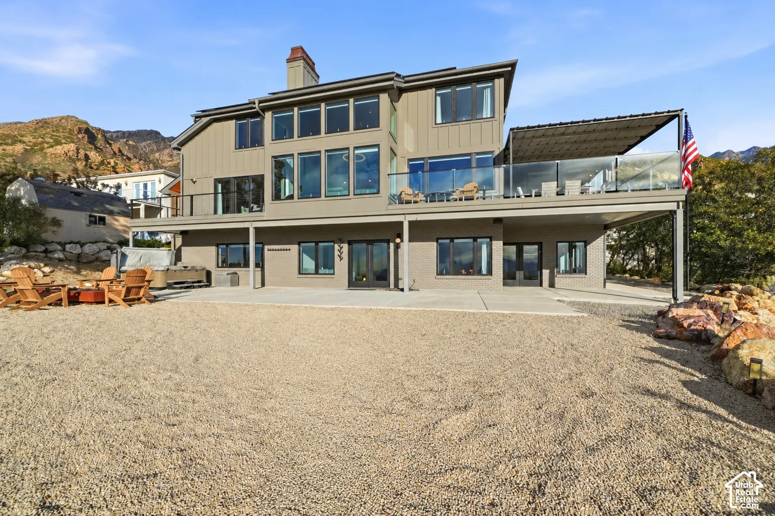 Multi-level residence featuring an upper-level balcony with glass railing, a covered lower patio, and a gravel-covered outdoor space
