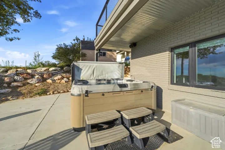 Concrete patio area featuring a built-in spa with steps, a stone retaining wall, and a brick exterior facade