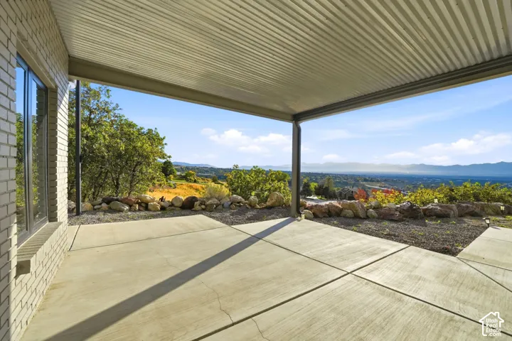 Expansive covered patio featuring a corrugated metal ceiling and concrete flooring, complemented by a brick exterior wall and large windows