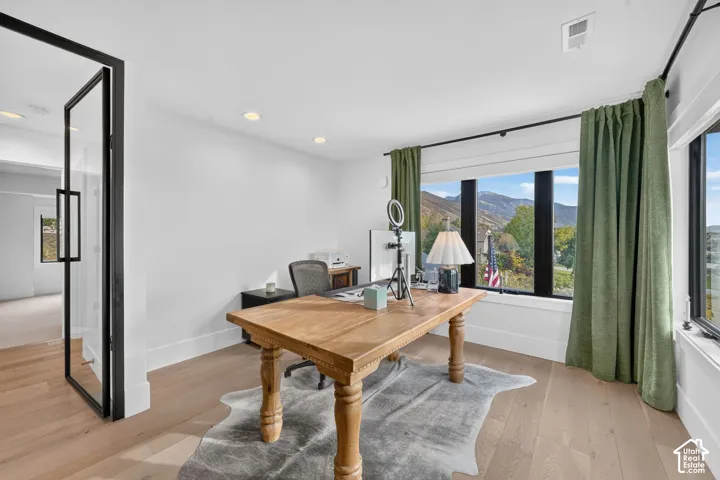 Light wood-finish flooring, recessed lighting, expansive windows with dark framing, and a full-light pivot door with dark framing