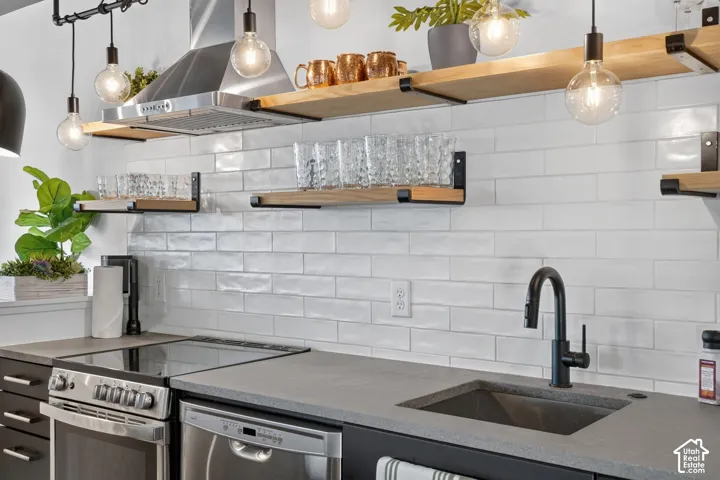 White subway tile backsplash, open wood shelving with black metal supports, stainless steel range hood, stainless steel dishwasher, and dark composite sink with a matte black faucet