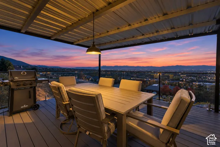 Expansive outdoor deck featuring a corrugated metal roof, suspended pendant lighting, composite decking, and glass panel railing