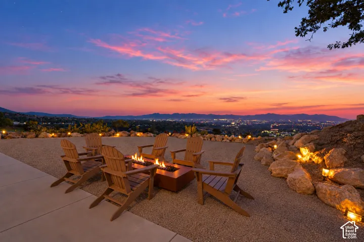 Outdoor patio featuring a built-in fire pit, multiple Adirondack chairs, gravel landscaping, and accent lighting