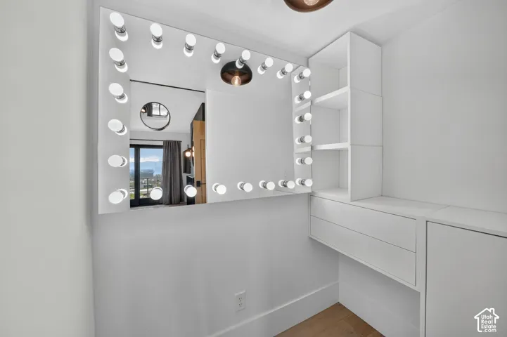 Built-in vanity area featuring a large illuminated mirror, integrated shelving, and white cabinetry with storage drawers