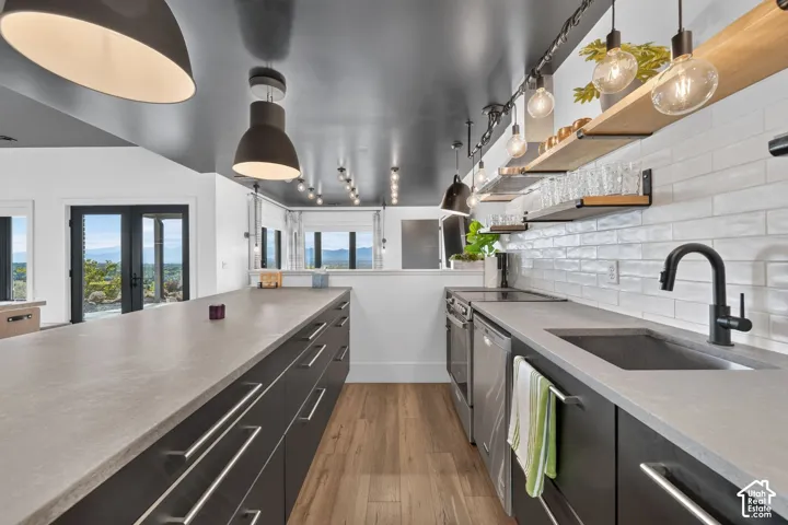 Expansive kitchen island with a stone-finish countertop, wood-finish flooring, black cabinetry with stainless hardware, subway tile backsplash, and a black gooseneck faucet