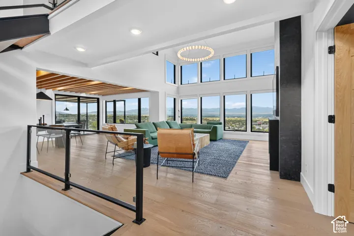 Expansive windows with mountain scenery, light wood-finish flooring, high ceilings, a built-in linear fireplace, and a glass and metal railing system