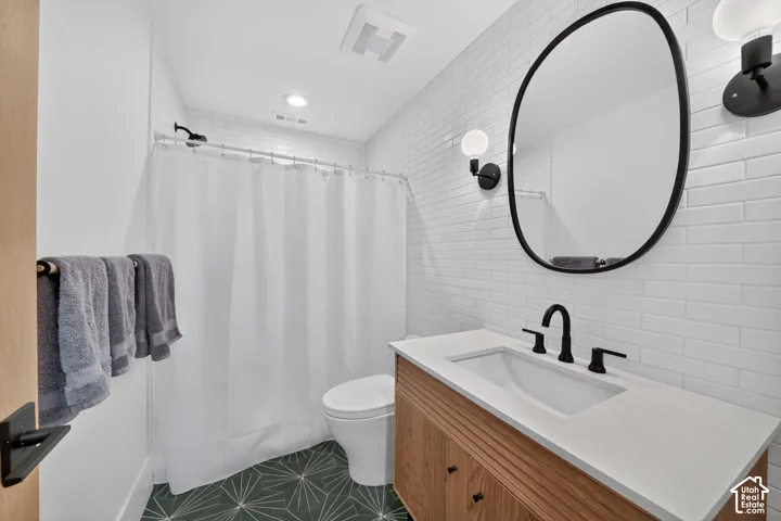 Bathroom featuring subway tile, wood-finish vanity with countertop sink, and patterned floor tile