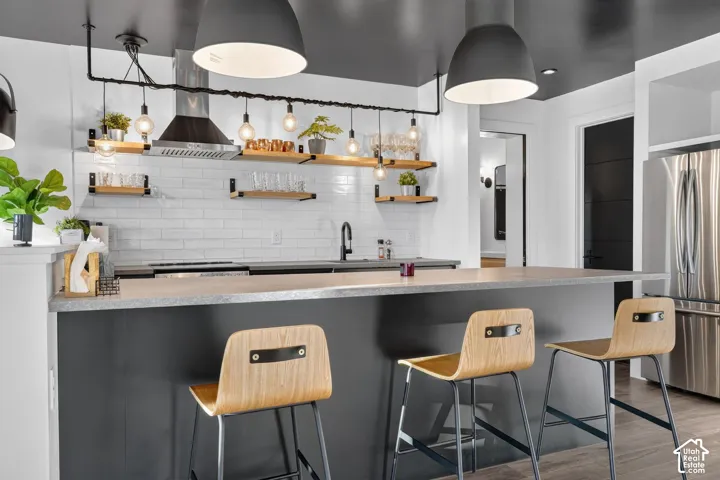 Kitchen featuring a stainless steel refrigerator, white subway tile backsplash, open shelving, and a large central island with a light-colored countertop