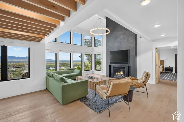 Vaulted ceilings with exposed wood beams, expansive floor-to-ceiling windows, modern fireplace with dark surround, light wood-finish flooring, and recessed lighting
