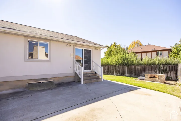 Concrete patio with direct access to the backyard, featuring a built-in stone fire pit, a mature privacy fence, and a manicured lawn