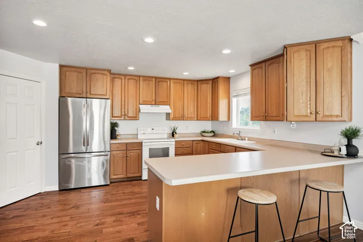 Kitchen featuring wood-finish flooring, ample cabinetry, stainless steel refrigerator, recessed lighting, and a breakfast bar