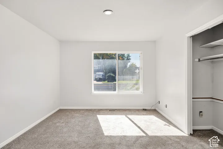 Recessed lighting, light gray wall finishes, gray carpet flooring, window with white trim, and a built-in closet with shelving and hanging rod
