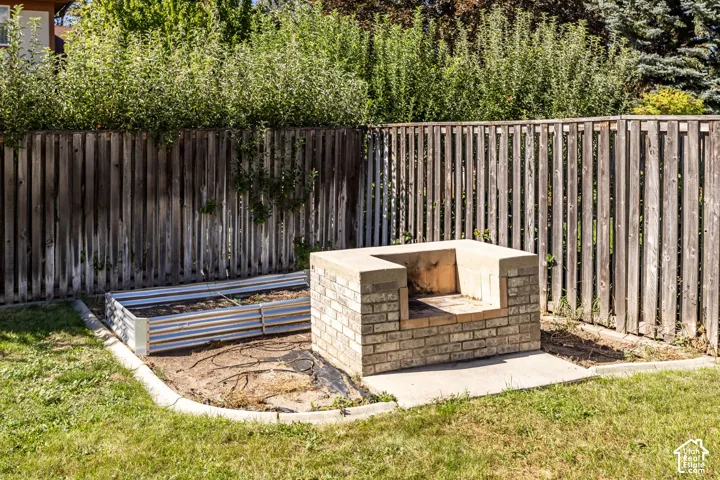 Brick outdoor cooking structure, raised garden bed, concrete border, and wood privacy fencing