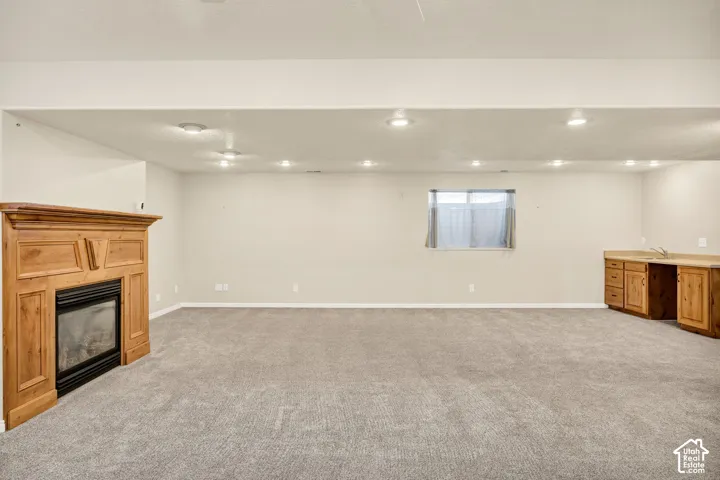 Recessed lighting illuminates a spacious room featuring a wood-mantled fireplace, neutral carpeting, and a built-in wet bar with wood cabinetry