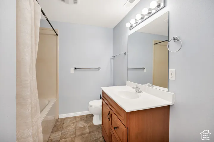 Bathroom featuring a wood-finish vanity with a white countertop, large wall mirror, and tile flooring