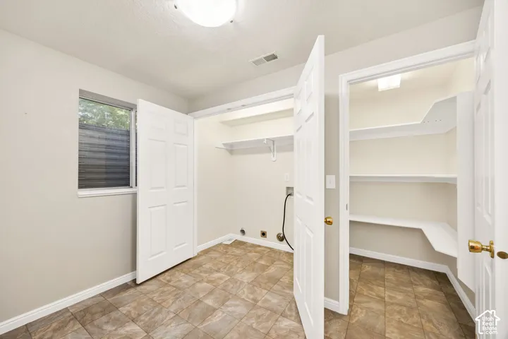 Laundry area with tiled flooring, built-in shelving, window with blinds, and additional storage closet with shelving