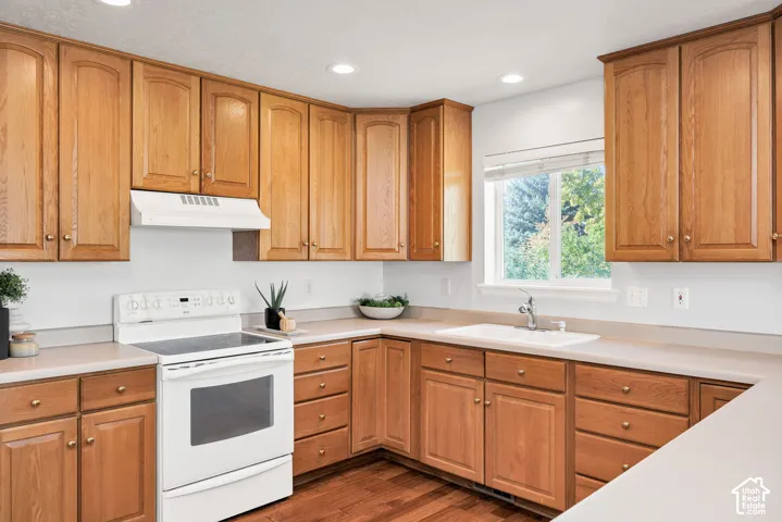 Wood-finish cabinetry, light-toned countertops, integrated white sink with chrome faucet, white electric range with matching range hood, recessed lighting
