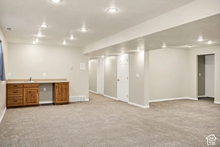 Expansive open-plan room with recessed lighting, light-toned carpeting, and a built-in wet bar with wood cabinetry and a neutral countertop