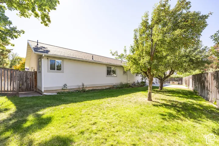 Expansive rear yard featuring green lawn, mature trees, and a wood-panel fence