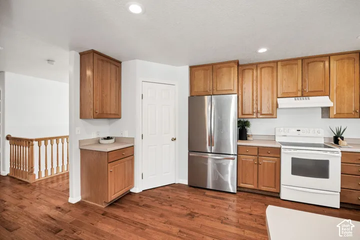 Kitchen featuring wood-finish cabinetry, stainless steel refrigerator, white electric range, and wood-finish flooring