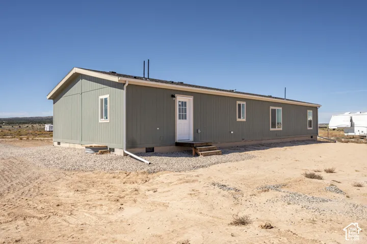 Sage green exterior siding, white frame windows, light-colored trim, white front door, and a gravel perimeter
