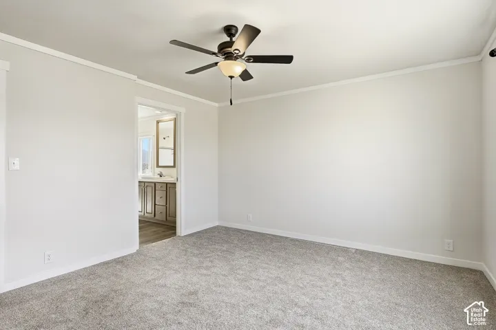 Neutral carpeting, ceiling fan with integrated lighting, crown molding, and a doorway opening to a bathroom with wood-finish flooring