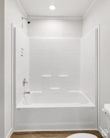 White bathtub with a chrome showerhead and faucet, surrounded by white subway tile and a recessed ceiling light