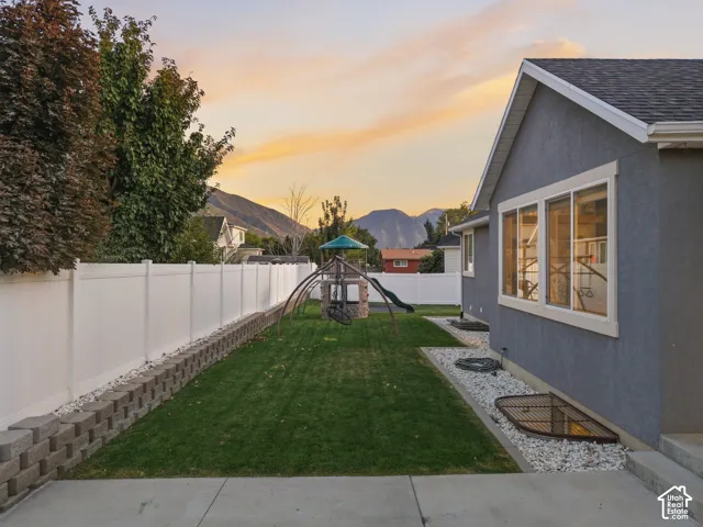 Expansive backyard with a manicured lawn, white privacy fencing, and a concrete patio