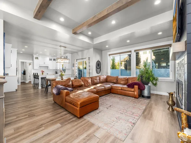 Vaulted ceiling with exposed wood beams, recessed lighting, wood-finish flooring, white cabinetry, and large windows