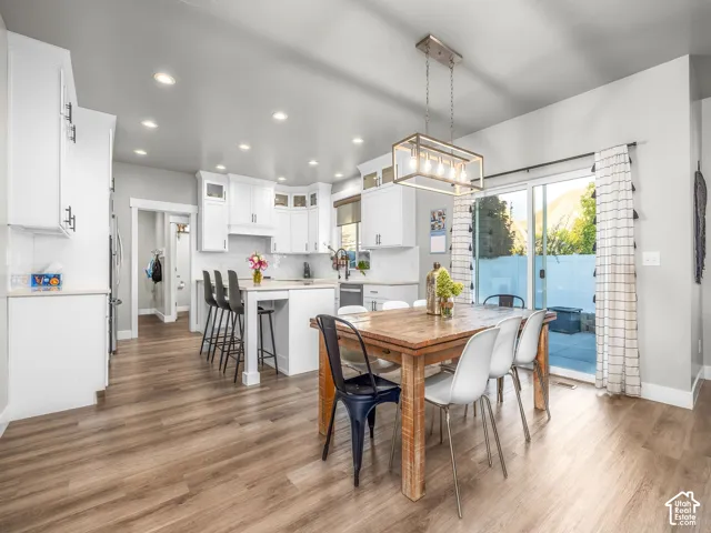 Open-concept kitchen and dining area featuring wood-finish flooring, white cabinetry, recessed lighting, and a contemporary linear chandelier