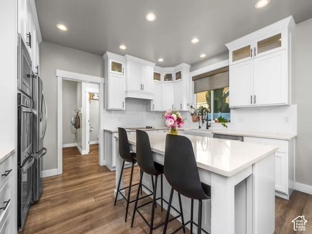 Modern kitchen featuring white cabinetry, light-toned countertops, wood-finish flooring, stainless steel appliances, and recessed lighting