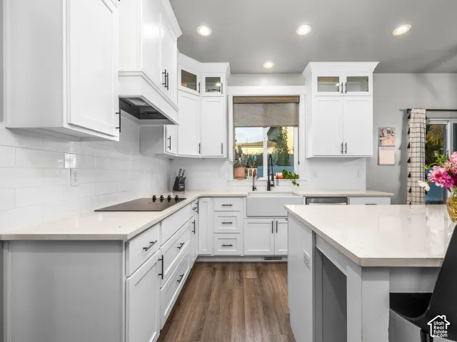 White shaker cabinetry with matte black hardware, light-toned countertops, white subway tile backsplash, wood-finish flooring, and a built-in cooktop