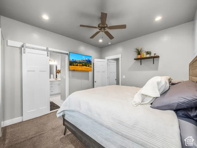 Recessed lighting, ceiling fan, carpet flooring, barn door entry to bathroom, and white cabinetry in bathroom