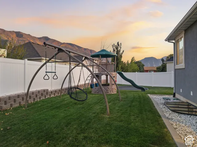 Expansive backyard featuring a manicured lawn, white privacy fencing, and a built-in playset