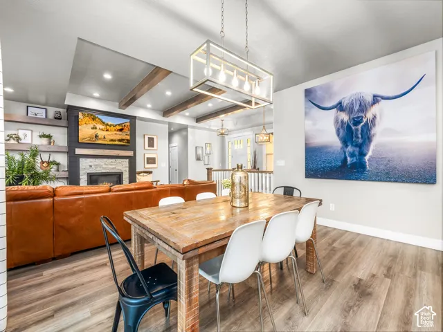 Open-concept living space featuring wood-finish flooring, a linear chandelier, a fireplace with a stone surround, and built-in shelving