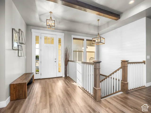 Entryway featuring wood-finish flooring, white shiplap accent wall, white spindle railing, and exposed ceiling beams
