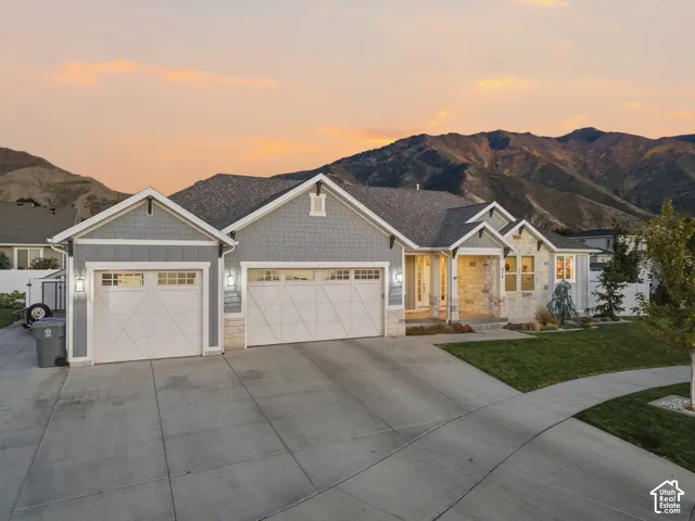 Stone and shingle exterior with a multi-car driveway, attached two-car garage, and a manicured lawn
