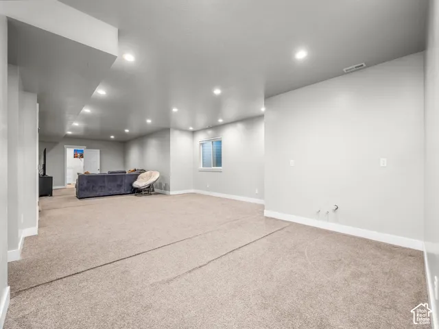 Spacious carpeted area with recessed lighting, a single window, and light-toned walls