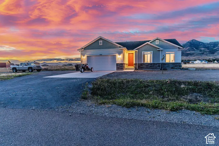 Contemporary exterior with light blue siding, stone facade accents, a prominent orange front door, a two-car garage, and a gravel driveway