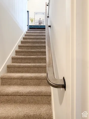 Carpeted staircase featuring a metal handrail with dark bronze brackets