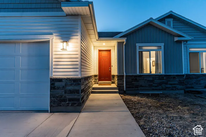 Red entry door, concrete walkway, stone veneer foundation, horizontal siding, and a paneled garage door