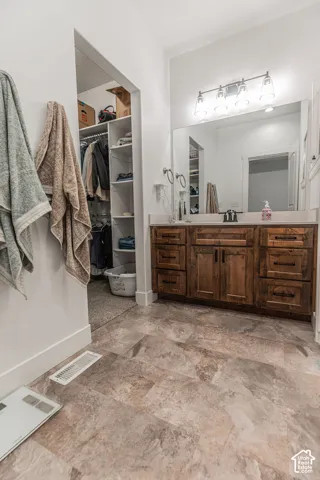 Wood-finish flooring, custom wood vanity with integrated sink, expansive mirror, and built-in closet shelving