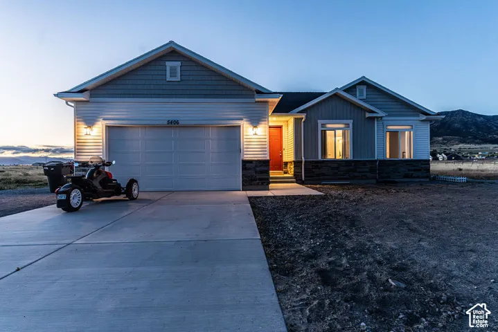 Ranch-style exterior with a two-car garage, concrete driveway, stone facade, and a vibrant red entry door