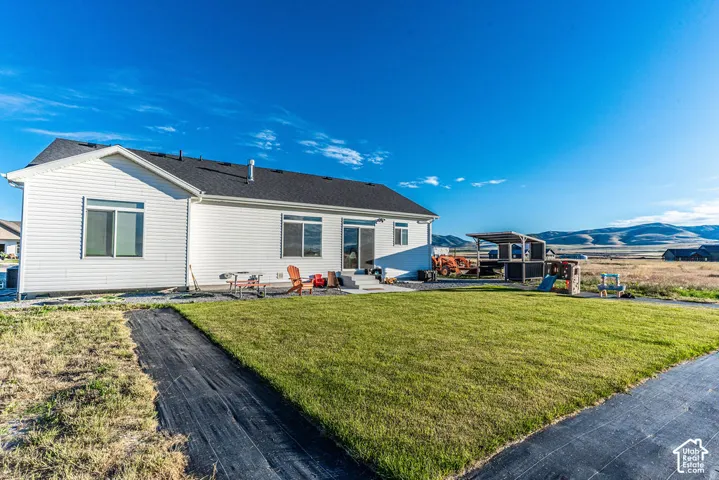 Rear exterior featuring white siding, a dark shingle roof, a concrete patio, and a grass lawn