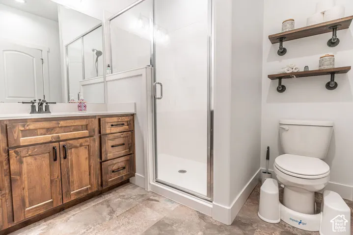 Wood-finish vanity with a light-toned countertop, glass-enclosed shower, wall-mounted shelving, and tiled flooring