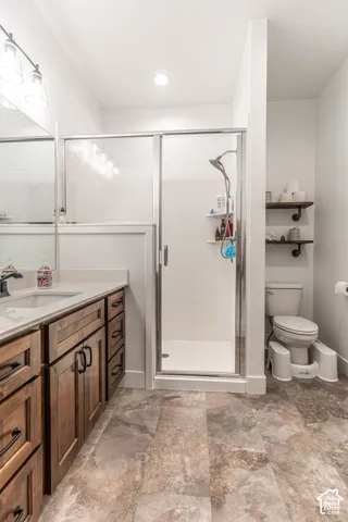 Bathroom featuring a single vanity with wood cabinetry, a white countertop, a walk-in shower with a glass enclosure, and patterned floor tiles