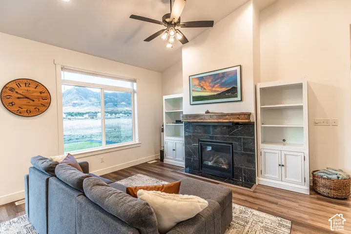 Spacious living area featuring a vaulted ceiling with a ceiling fan, a large picture window, and wood-finish flooring