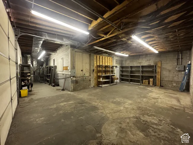 Concrete flooring, exposed wood beam ceiling, fluorescent lighting, concrete block walls, overhead garage door