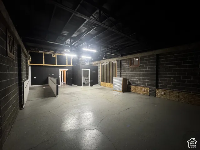 Exposed ceiling rafters with overhead lighting, concrete flooring, and exposed brick walls